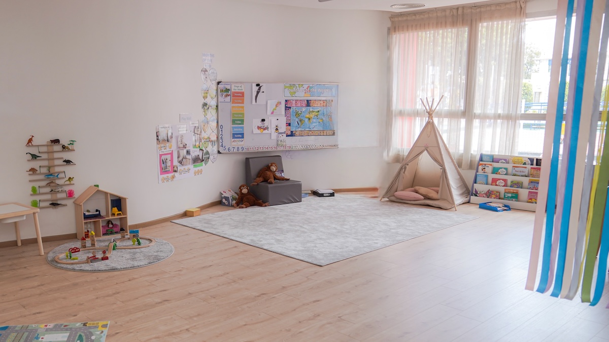 A calm, well-organised nursery classroom — soft furnishings, natural materials, clear and uncluttered spaces, child-height shelving. An environment that feels held and intentional rather than chaotic or institutional.